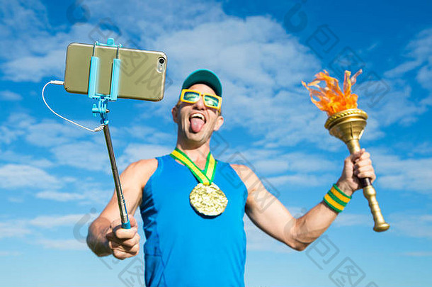微笑的运动员手持运动火炬在自拍棒上用手机自拍