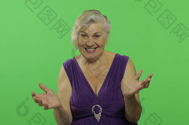 一位老妇人露出惊讶、喜悦和微笑。穿着紫色连衣裙的快乐的老奶奶。放置您的徽标或文字。色度键。绿色屏幕背景