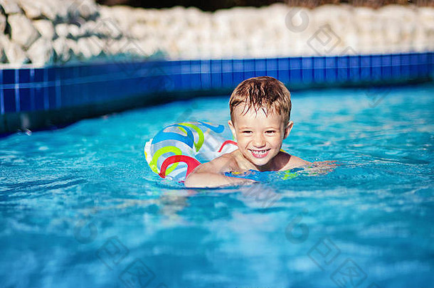 带着戒指在游泳池里游泳的快乐的小男孩。进入度假村