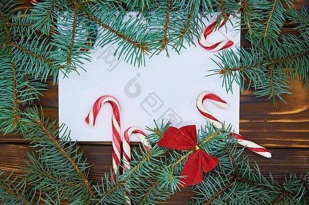 在一张木质背景的白纸上，周围是蓝云杉树枝和圣诞糖果。