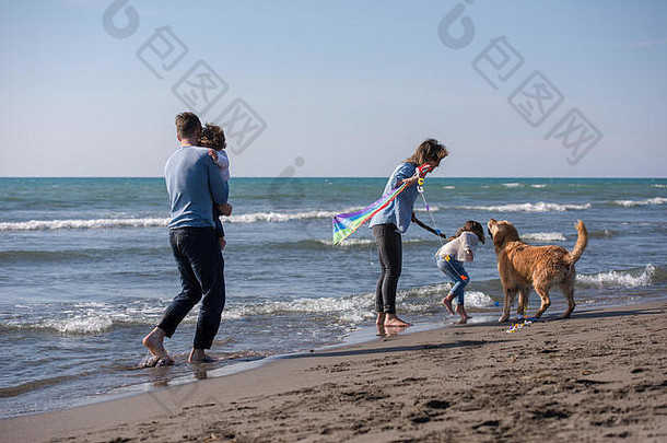 秋天，一个快乐的小家庭和孩子们在海滩上玩狗和风筝