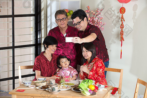 庆祝中国新年，吃团圆饭。快乐亚洲华人多代同堂用餐时身着红色旗袍自拍