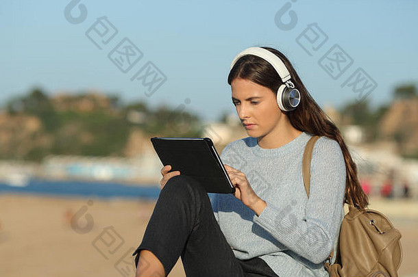 坐在海滨小镇的海滩上，用平板电脑和耳机进行严肃的女孩电子学习
