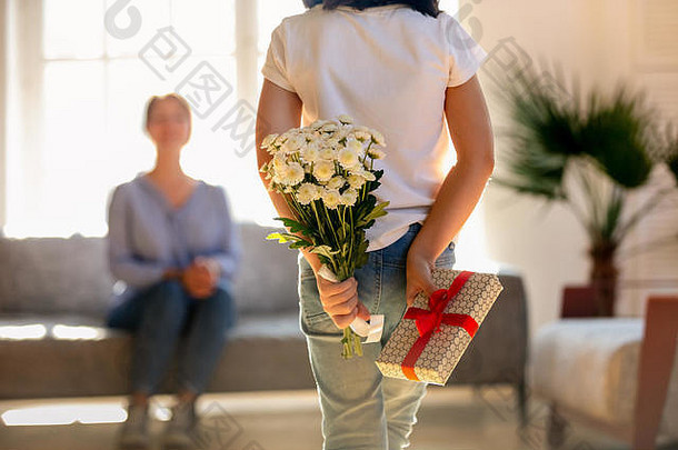 抱着鲜花和礼品盒的小女儿的后视图