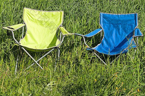 阳光明媚的日子里，绿草地上有两张空折叠椅