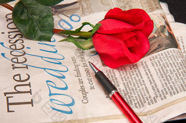 报纸的特写镜头，上面放着红玫瑰和钢笔