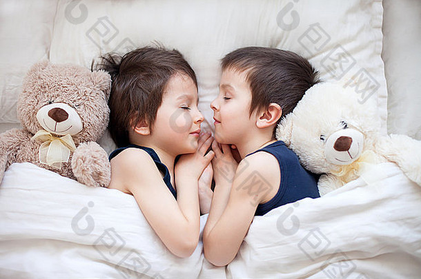 两个男孩抱着泰迪熊，躺在床上，下午睡觉，拥抱着玩具