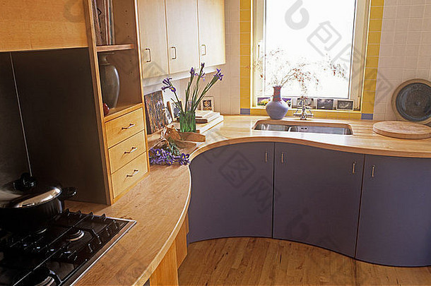 淡紫色厨房单元上的浅木成型工作台面上的<strong>燃气灶</strong>，窗户下方设有水槽