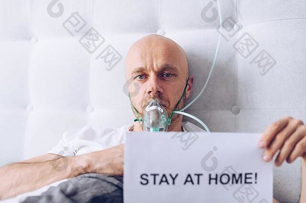 病人通过氧气面罩呼吸，并持写有“呆在家里”信息的卡片
