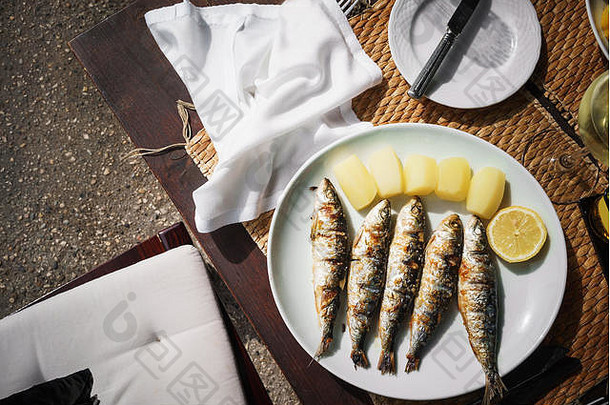 油炸开胃鲭鱼、一片柠檬和黄土豆放在一个白色盘子上，放在一张木桌上。桌子上有一张白色的餐巾