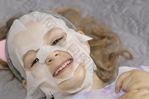 躺在床上，脸上戴着布制保湿面膜的青<strong>春</strong>期前可爱女孩。儿童小孩用织物<strong>化妆</strong>品面膜护理皮肤。温泉。干净、健康。<strong>美容</strong>治疗。皮肤护理