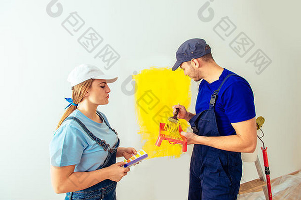一对穿着工作服的年轻夫妇用画笔把墙刷成黄色