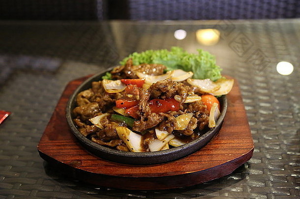 这是一幅由牛肉、辣椒和蔬菜在热铁板上烹制而成的中国菜的图像。