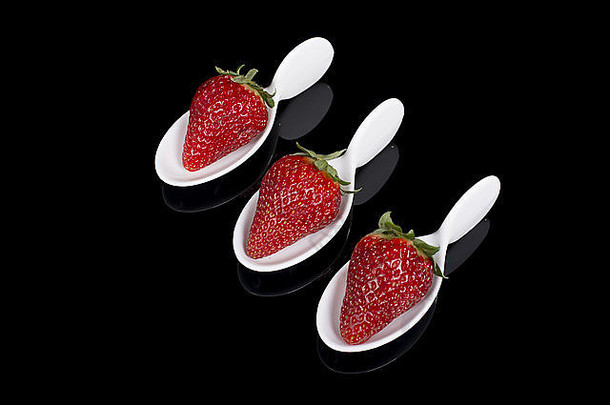放在玻璃盘子上的三个装在彩陶勺里的草莓