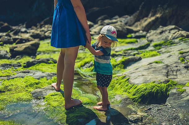 一个阳光明媚的夏日，一位年轻的母亲带着她的孩子在岩石海滩上散步