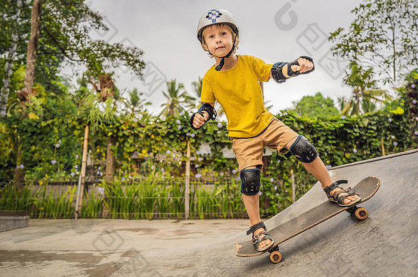 一个戴着头盔和护膝的运动男孩在溜冰场里学习滑板。儿童教育、体育