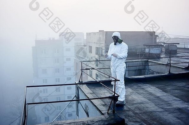 研究员穿白色保护包罗万象的手套气体面具持有手玻璃瓶蓝色的试剂镊子块公寓背景