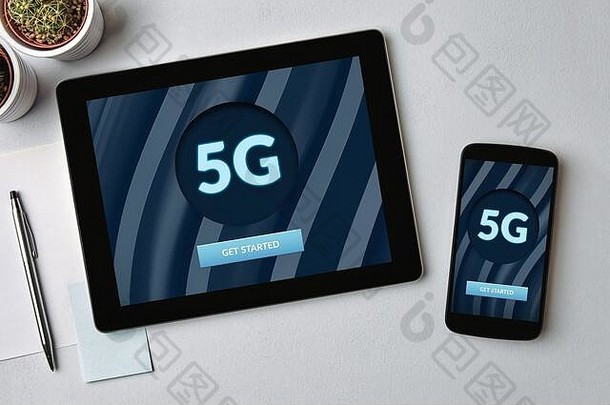 平板电脑和手机屏幕上的5G网络概念，灰色桌面。俯视图