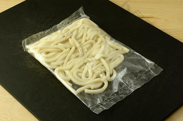 黑砧板上的新鲜生乌冬面包装，用于制作卤面