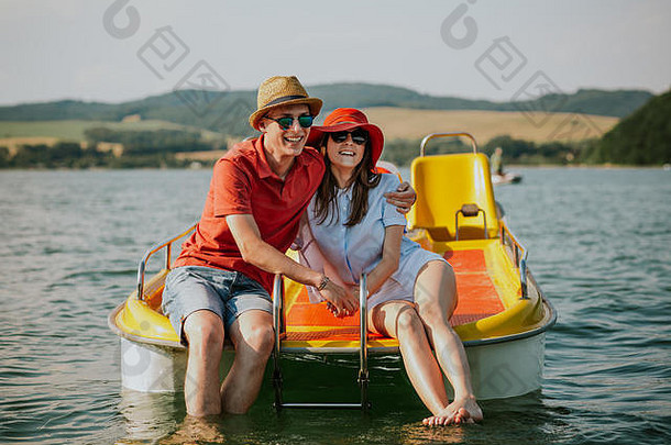 坐在脚踏船上微笑的年轻夫妇的正视图。在湖面上享受划船乐趣的男女肖像。