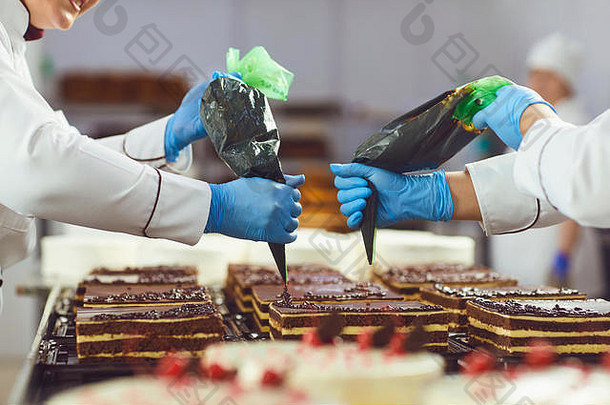 在一家面包房里，糖果商在巧克力蛋糕上装饰袋子里的奶油。
