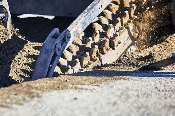 挖沟机链条运动的特写镜头在泥土中挖沟，工人铲到一边