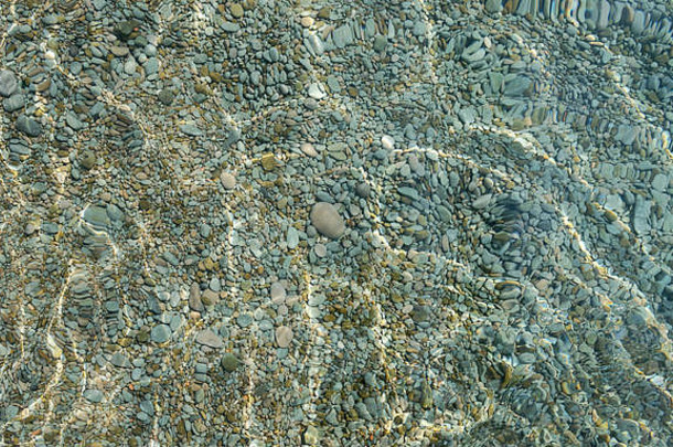 闪烁的阳光照射在卵石海床上，在浅滩清澈的海水下作为自然背景。