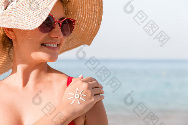 海滩上手上有防晒霜做成的太阳形状的年轻女子。