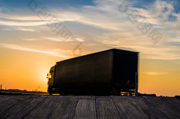 空的乡村木桌面，运动模糊的卡车在日落的背景下。可以蒙太奇或显示您的产品。