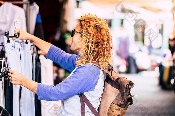 快乐的旅行者年轻的金发女郎卷曲的女人选择衣服市场替代假期购物生活方式概念