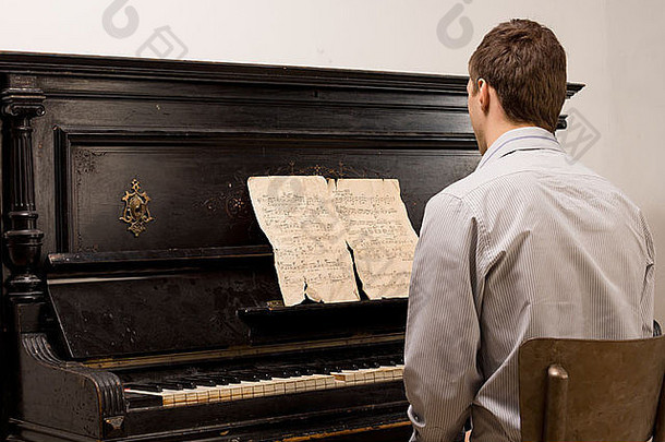 一个年轻人坐在钢琴上演奏着一首破旧的乐谱，怀旧的一刻，从后面望去