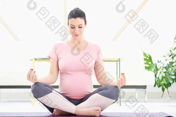 孕妇在家中以瑜伽姿势冥想的全长照片。