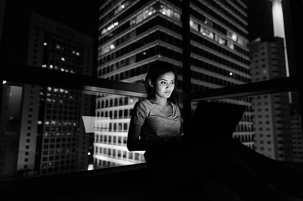 年轻的美丽的亚洲女人移动PC玻璃窗口视图城市晚上