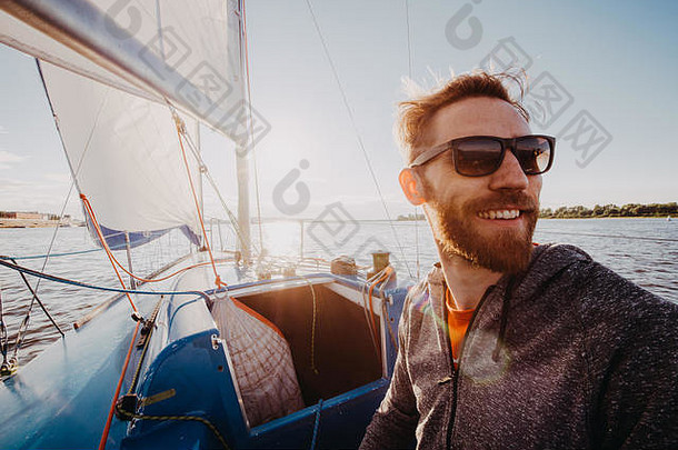 一名男子穿着休闲服，戴着墨镜在游艇上。快乐大胡子游艇驾驶员特写肖像。船上英俊的水手在海上或河流上的<strong>盛典</strong>中微笑。