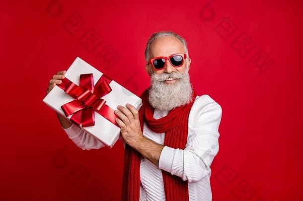 酷炫的圣诞老人模样的男人带着大礼物盒，戴着太阳眼镜，针织套衫，红色背景，迎接新年