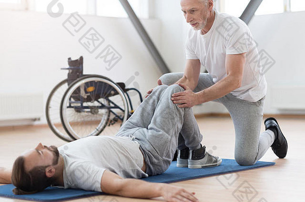 熟练的老年骨科医生在健身房为残疾人伸展身体