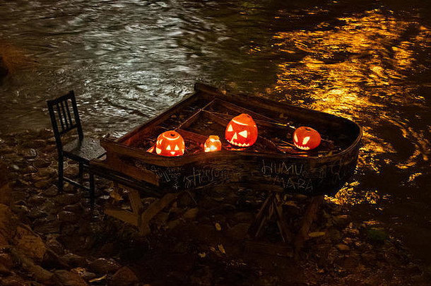 鬼祟祟的万圣节南瓜，杰克O灯笼，在一架老式大钢琴上点着蜡烛，背景是河流