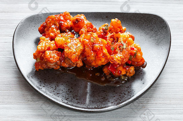 中式<strong>韩国料理</strong>-上图：黑色盘子上的Kkanpunggi辣蒜香炸鸡片和甜酱蔬菜特写