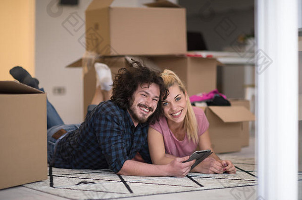 相爱的年轻夫妇搬进新公寓，躺在地板上，在平板电脑上上网，寻<strong>找</strong>新的<strong>装修</strong>创意