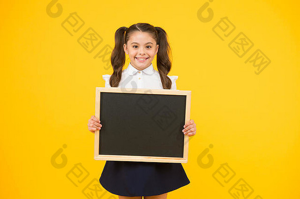小广告制作人。拿着黄色背景黑板的小学生。戴着学校广告黑板的小孩。小女孩用空黑板为你的文字，空间。