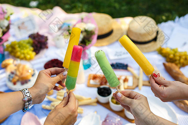 在夏日野餐的背景下，女人手拿着五颜六色的冰激凌棒。夏季周末。