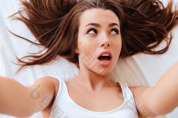 一位美丽的黑发女子躺在床上自拍的特写照片