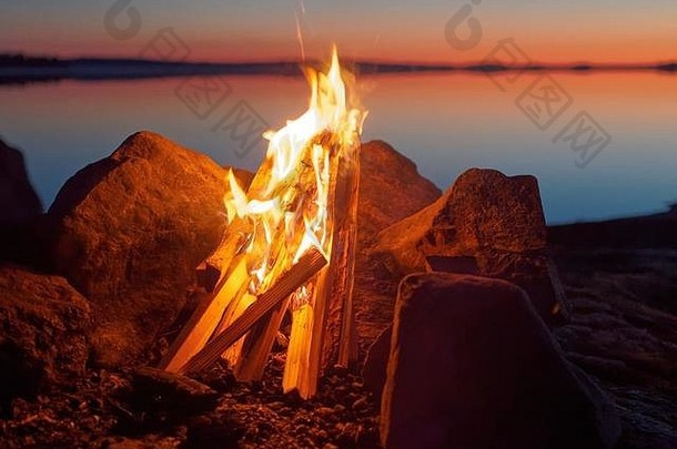 夜间海滩上的篝火和大气中的火焰。湖底的静水，太阳的暖色