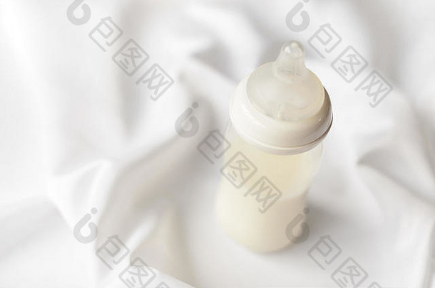 在白色丝绸缎子背景上为新生儿提供一瓶牛奶。免费拷贝空间。<strong>妇幼保健</strong>概念。