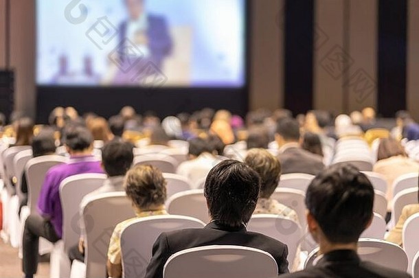 在会议厅或研讨会的舞台上聆听演讲者演讲的观众后视图，关于投资理念的商业和教育