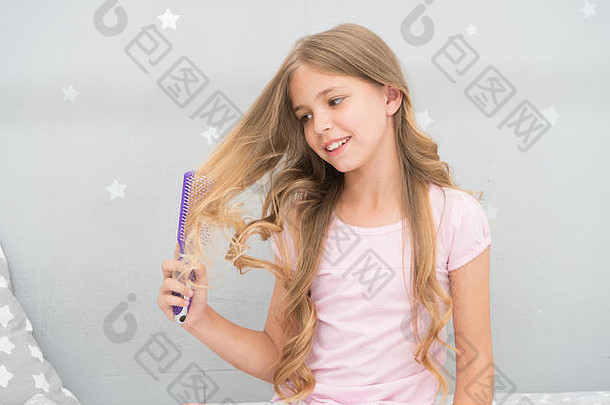 孩子卷曲的发型持有毛刷梳子应用石油梳理头发健康的头发护发素面具有机石油梳子头发美沙龙提示女孩长卷曲的头发灰色室内背景