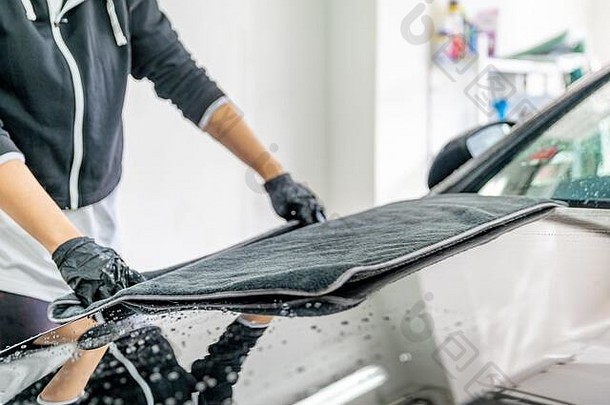 用超细纤维布擦拭汽车引擎盖上的水。手洗豪华轿车