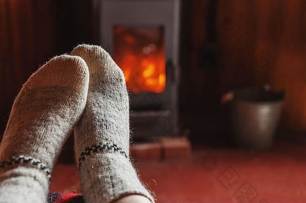在壁炉背景下穿着冬衣和羊毛袜子的脚。在冬天或秋天的晚上，坐在家里放松和热身的女人。冬季和寒冷天气概念。圣诞夜