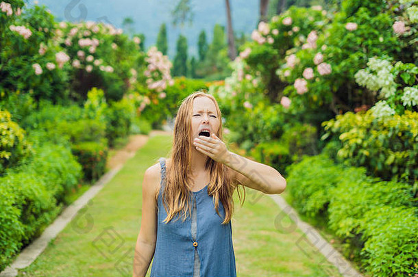 年轻的女人打喷嚏公园背景开花树过敏花粉概念