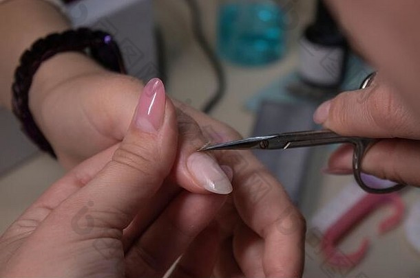 修指甲的过程。专业美甲师手部特写，在沙龙去除角质层。修指甲和指甲清洁的概念。美的概念。虫胶凝胶上光剂